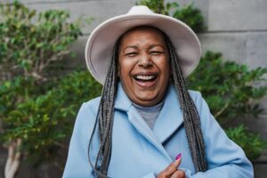 Older woman in blue coat and hat laughs and smiles