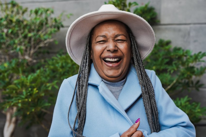 Older woman in blue coat and hat laughs and smiles