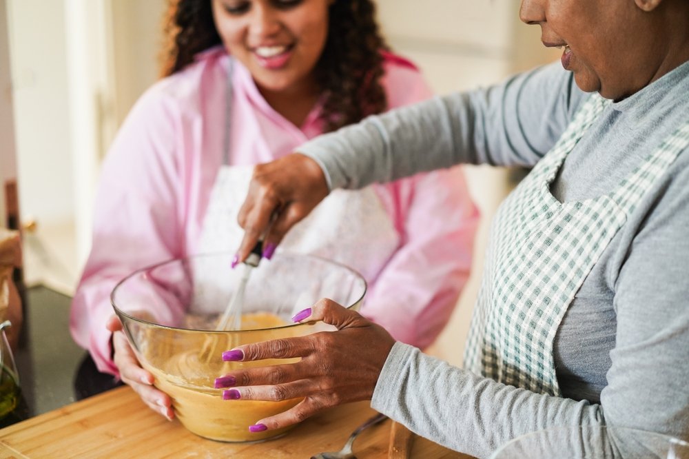 A senior woman and her caregiver cook together in the kitchen