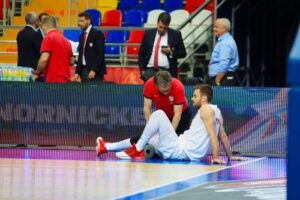 Basketball player on court with athletic trainer in in the background