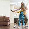 Joyful grandmother dancing and smiling while having fun together with her little granddaughter in a living room at home.