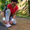 Active middle-aged woman runner, African American athlete tying shoelaces getting ready for jog along the forest park on a warm sunny summer day.